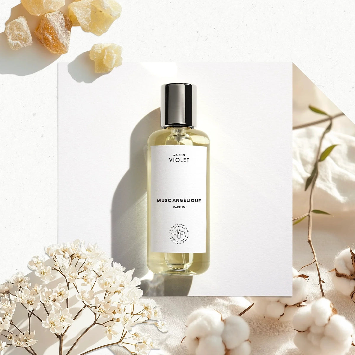 Musc Angélique by Maison Violet perfume bottle styled with cotton and white blossoms on bright background