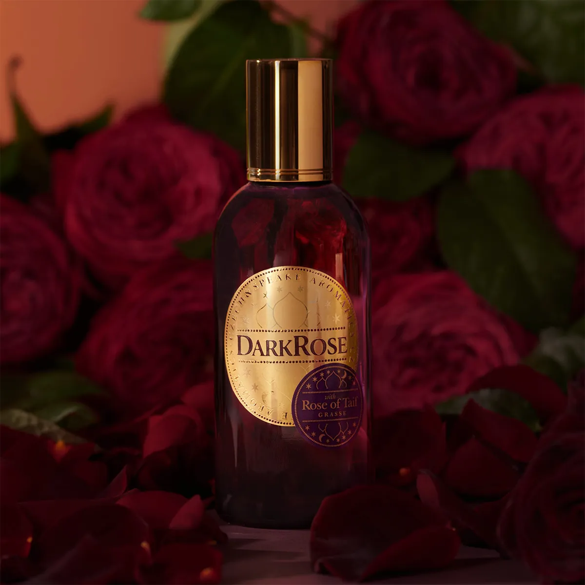 Bottle of DarkRose perfume surrounded by dark red roses